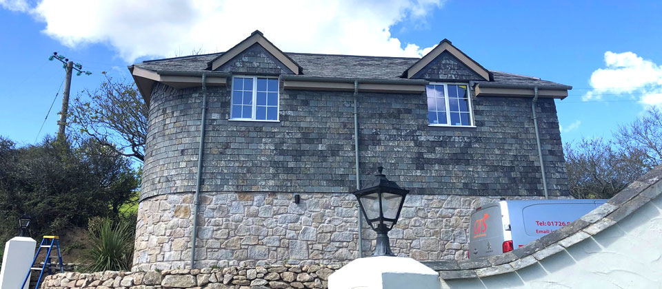 Reclaimed slate roof with dormer windows and adjacent metal roofing on a stone house